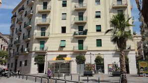 Un edificio de varios pisos con balcones, un acceso cubierto y una palmera.