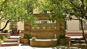 Un patio con una fuente de ladrillo, plantas en macetas y mobiliario exterior.