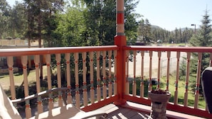 Une terrasse en bois avec une balustrade, un bac à fleurs en pierre et une vue sur un parc arboré avec une aire de jeux.