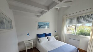 A bedroom with a bed, two bedside tables, a window with blinds, and a painting on the wall. - ANDERNOS, 8 PERSONS VILLA 140M2 PETS WELCOME (Andernos-Les-Bains)