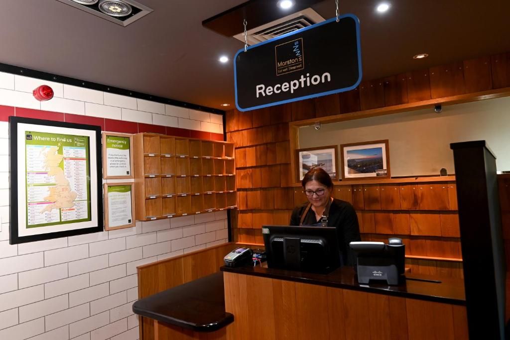 Zona de recepción con un cartel que indica 'Reception', un mostrador con una computadora y una pared decorada con cuadros enmarcados y carteles informativos.