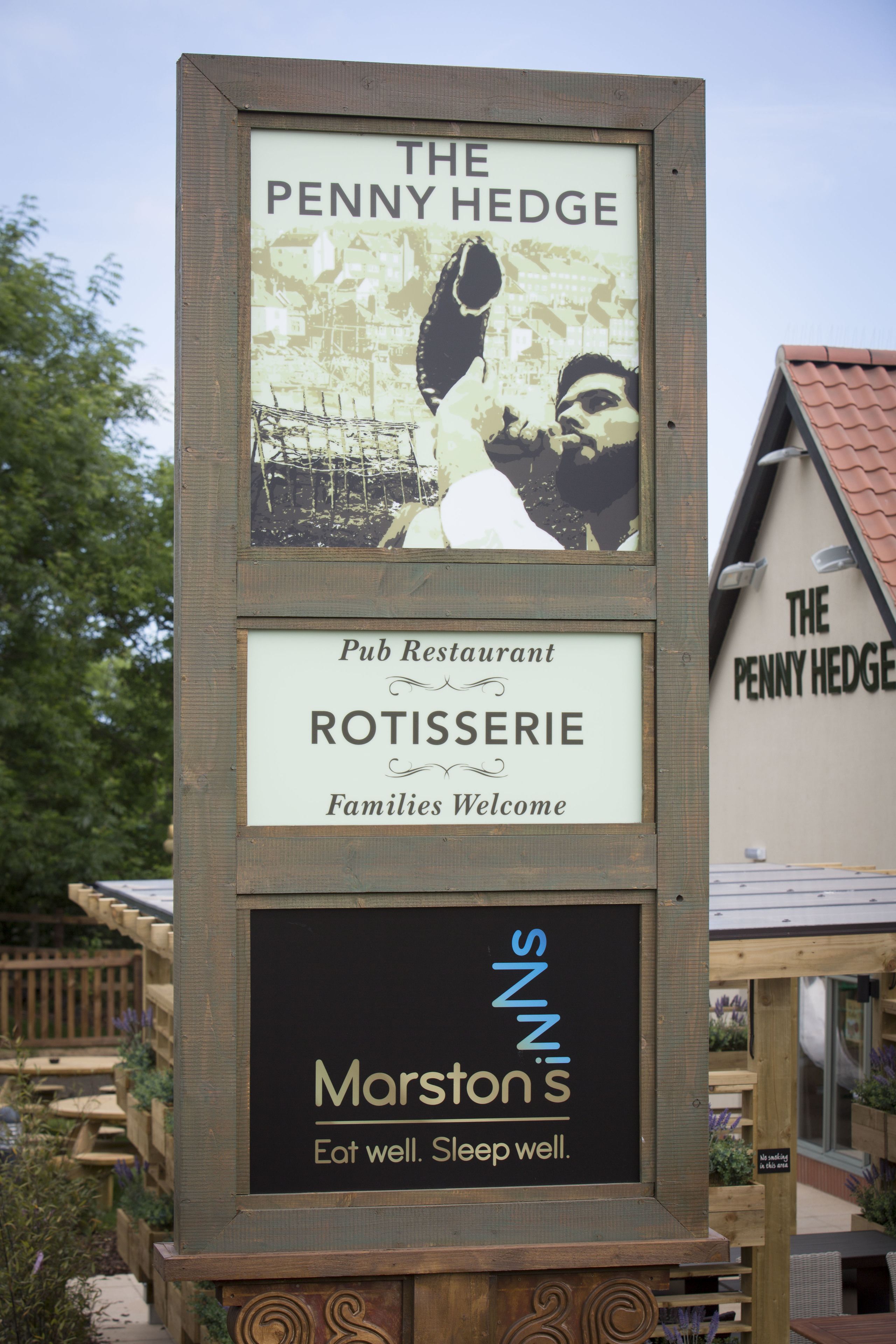 A signboard for The Penny Hedge Pub Restaurant, featuring a family-friendly welcome message and a slogan for Marston's.