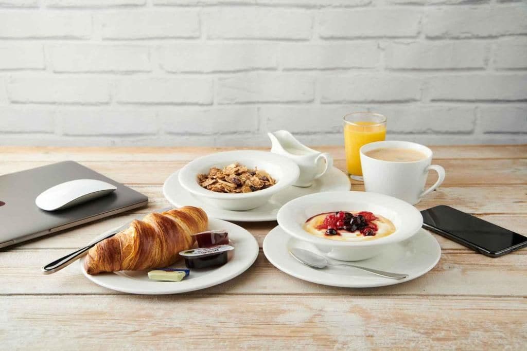 Aamiaispöytä, jossa on puupöydällä croissantteja, muroja, kahvia ja mehua.