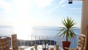 Et rundt bord med stole, en potteplante og en lygt på en balkon med havudsigt.