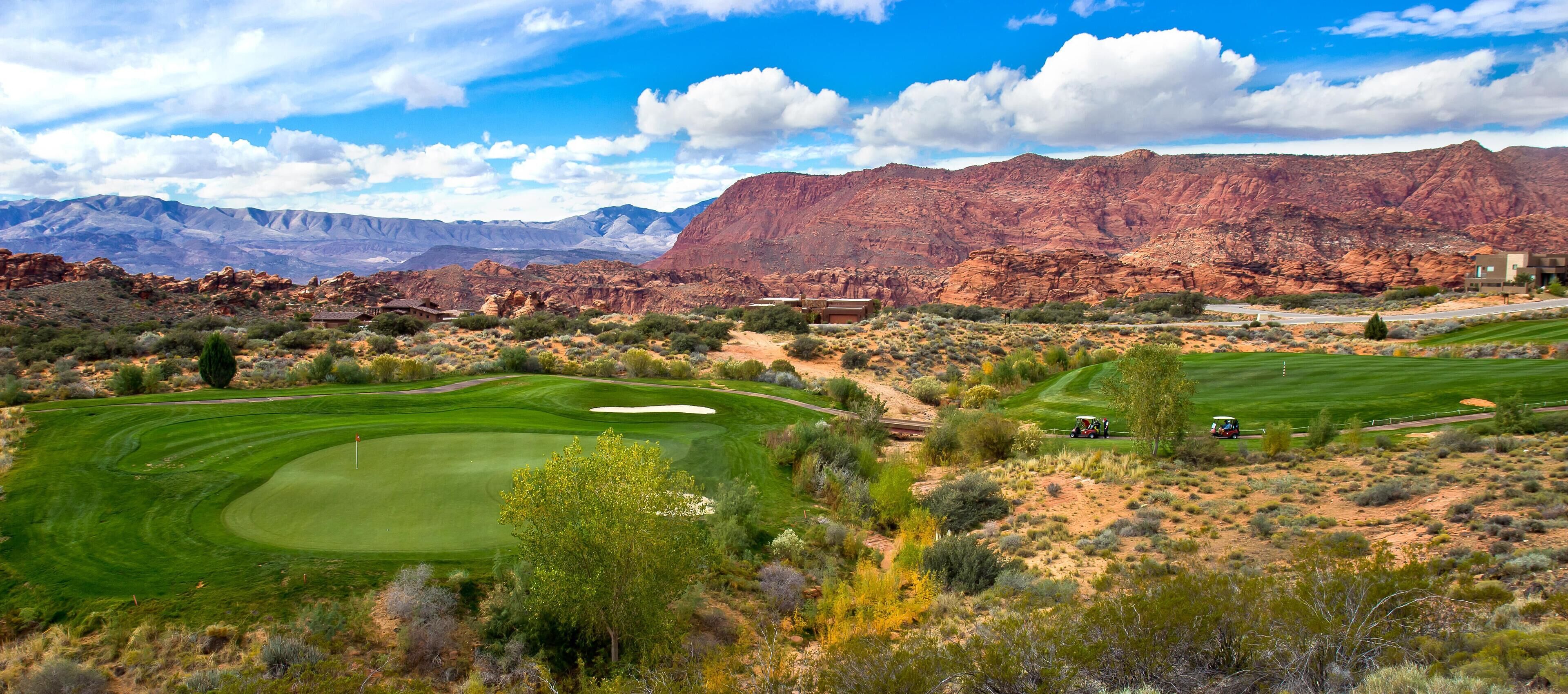 A golf course with a desert landscape, mountains, and a clear sky.