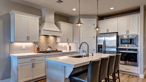 A modern kitchen with white cabinetry, stainless steel appliances, and a central island with bar stools. - Livin On The Ledge (St. George)