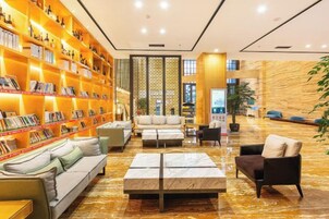 Un hall de hotel con una gran estantería, una zona de estar y una pared decorativa.