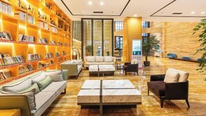 A modern lobby with a marble floor, a sofa, a coffee table, and a bookshelf filled with books. - Times Holiday Hotel (Liupanshui)