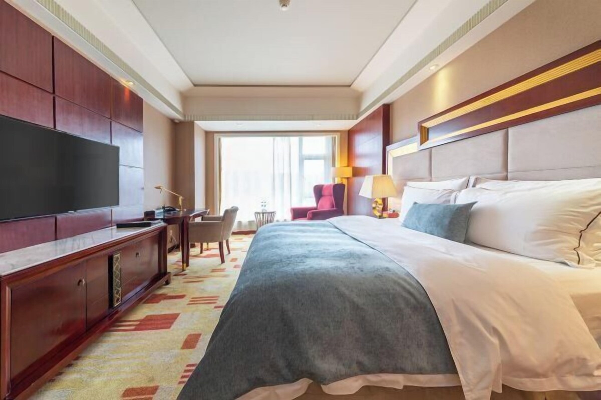 A hotel room with a large bed, a TV, a desk, and a chair.