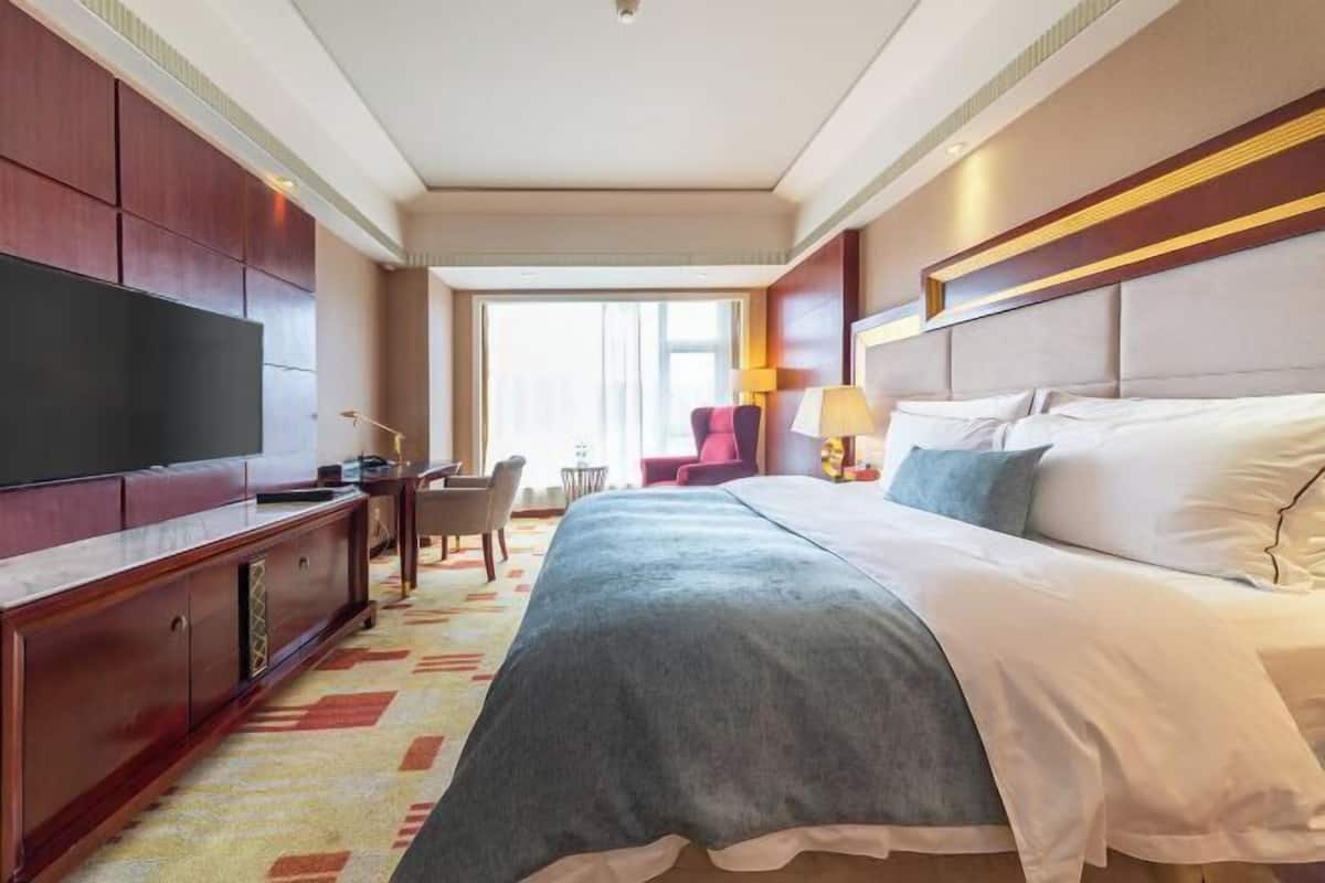 Hotellihuone, jossa on suuri sänky, televisio, työpöytä ja tuoli.