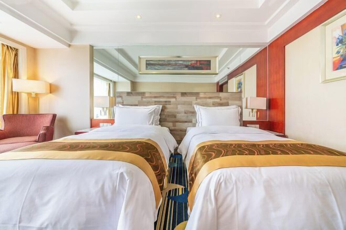 A hotel room with two beds, a sofa, a painting, and a lamp.