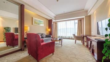 A hotel room with a red armchair, a sofa, a TV, a desk, and a large window.