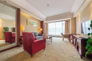 A hotel room with a red armchair, a sofa, a TV, a desk, and a large window.