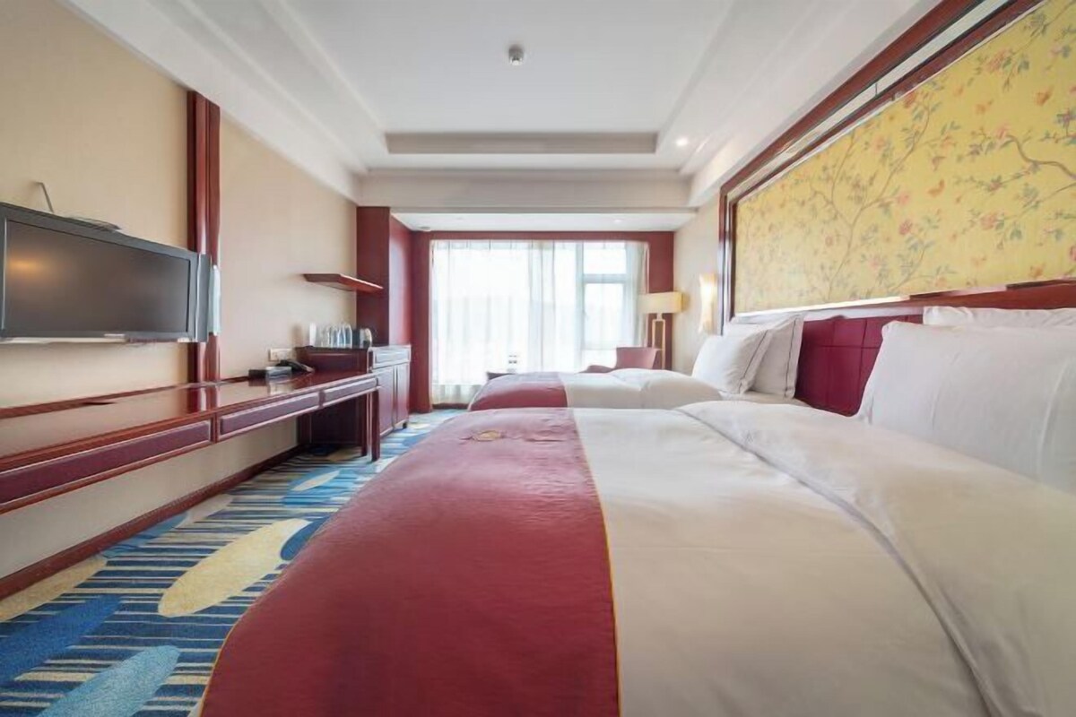 A hotel room with a large bed, a television, a desk with a computer, and a window with curtains.