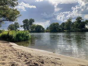 A riverbank with a sandy beach, dense greenery, and trees in the background. - Apartment in the nature and star park Westhavelland (Havelaue OT Wolsier)