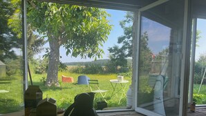 Une véranda donnant sur un espace verdoyant, un arbre et du mobilier d’extérieur.