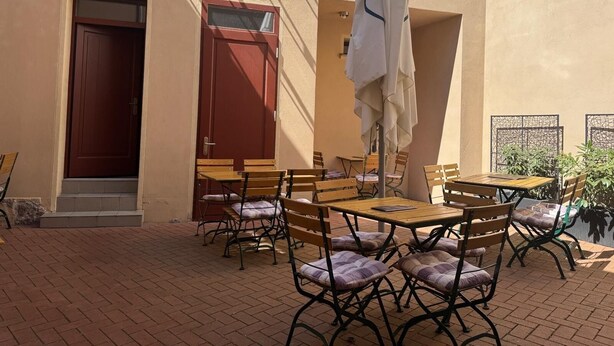 An outdoor patio with multiple wooden tables and chairs, a white umbrella, and a red door. - Gästehaus Innfernow (Fürstenberg-Havel)