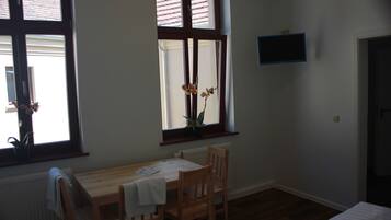Une pièce avec une table et des chaises en bois, une fenêtre donnant sur un paysage agréable, un radiateur et un téléviseur fixé au mur.