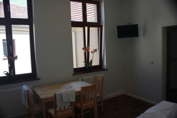 A room with a wooden table and chairs, a window with a view, a radiator, and a wall-mounted TV. - Gästehaus Innfernow (Fürstenberg-Havel)
