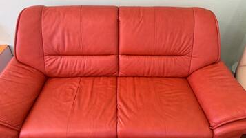 A red leather sofa with a cushioned backrest and armrests.