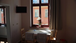 A room with a wooden table and chairs, a potted plant, and a window with a view of a building. - Gästehaus Innfernow (Fürstenberg-Havel)