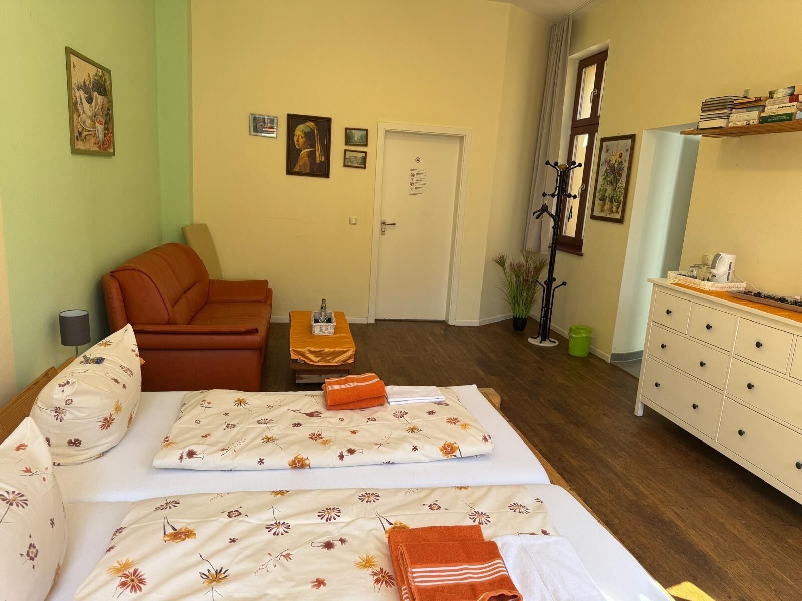 A hotel room with a bed, a sofa, a small table with a bottle, a dresser, and a door.