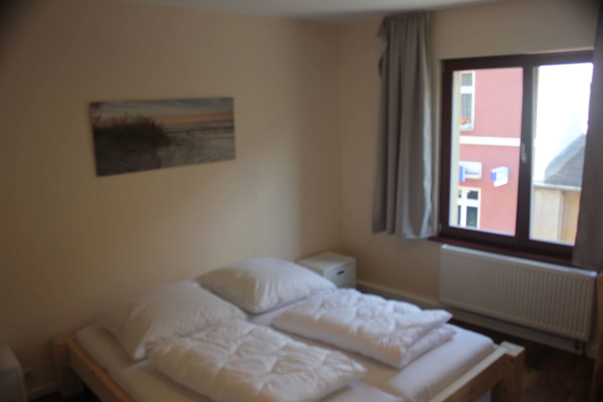 A bedroom with a bed, a nightstand, a window, and a painting on the wall.