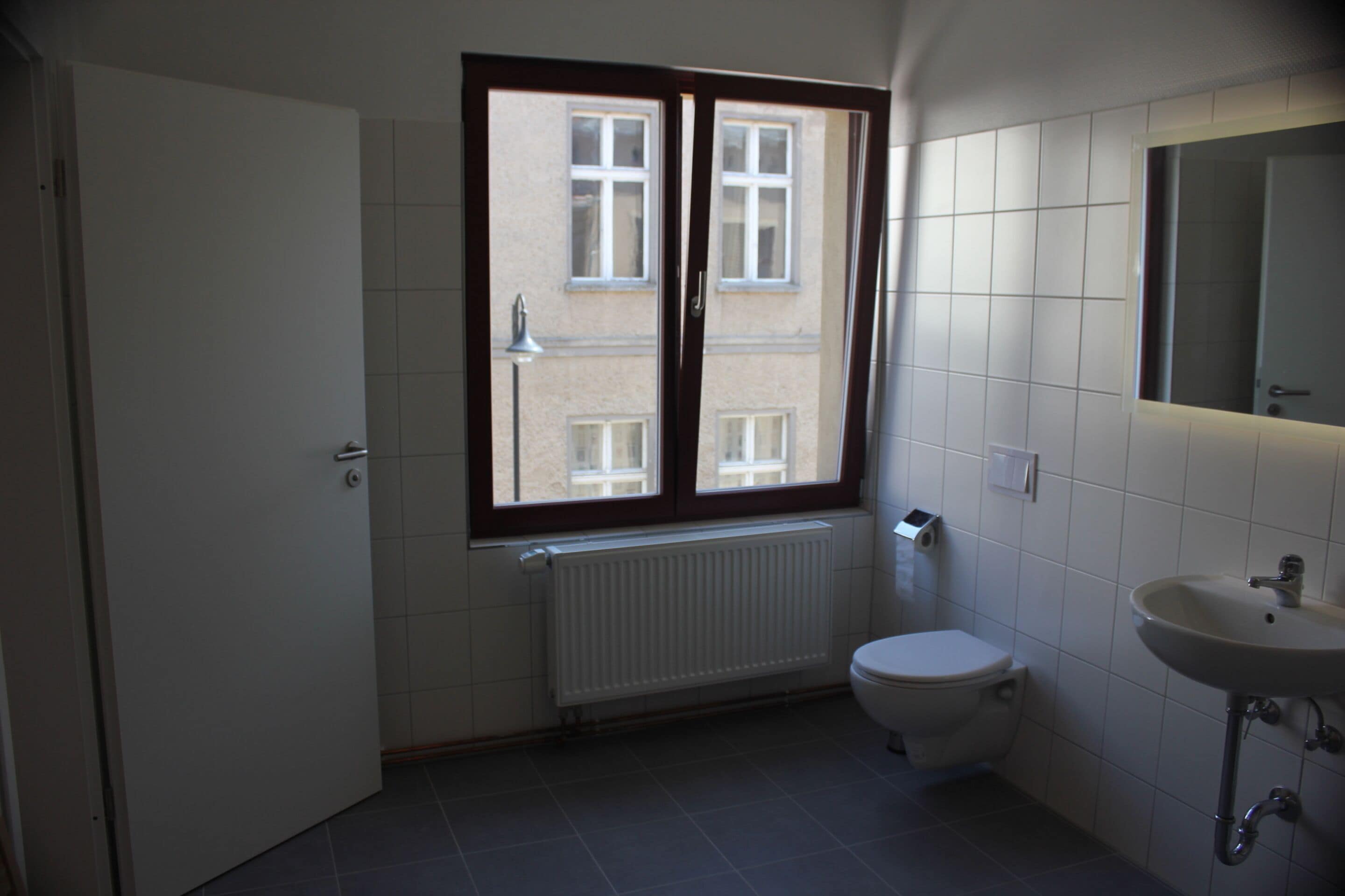 Un baño pequeño y limpio con inodoro, lavamanos y ventana con vistas a edificios.