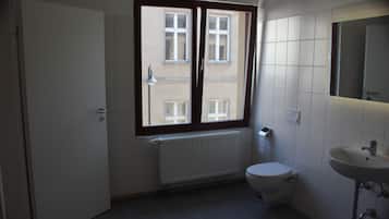 Un baño pequeño y limpio con inodoro, lavamanos y ventana con vistas a edificios.