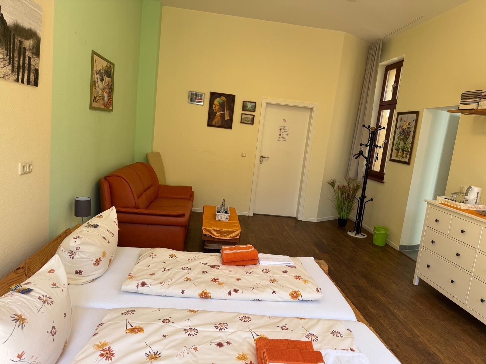 A room with a bed, a sofa, a small table with a bottle, and a dresser.