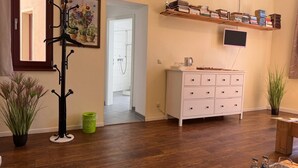 A room with a wooden floor, a white dresser, a TV mounted on the wall, a coat rack, and a hallway leading to a bathroom. - Gästehaus Innfernow (Fürstenberg-Havel)