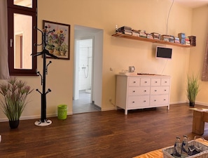 A room with a wooden floor, a white dresser, a TV mounted on the wall, a coat rack, and a hallway leading to a bathroom. - Gästehaus Innfernow (Fürstenberg-Havel)