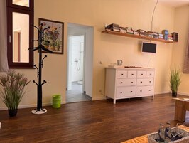 Una habitación con piso de madera, un aparador blanco, un televisor montado en la pared, un perchero y un pasillo que conduce a un baño.