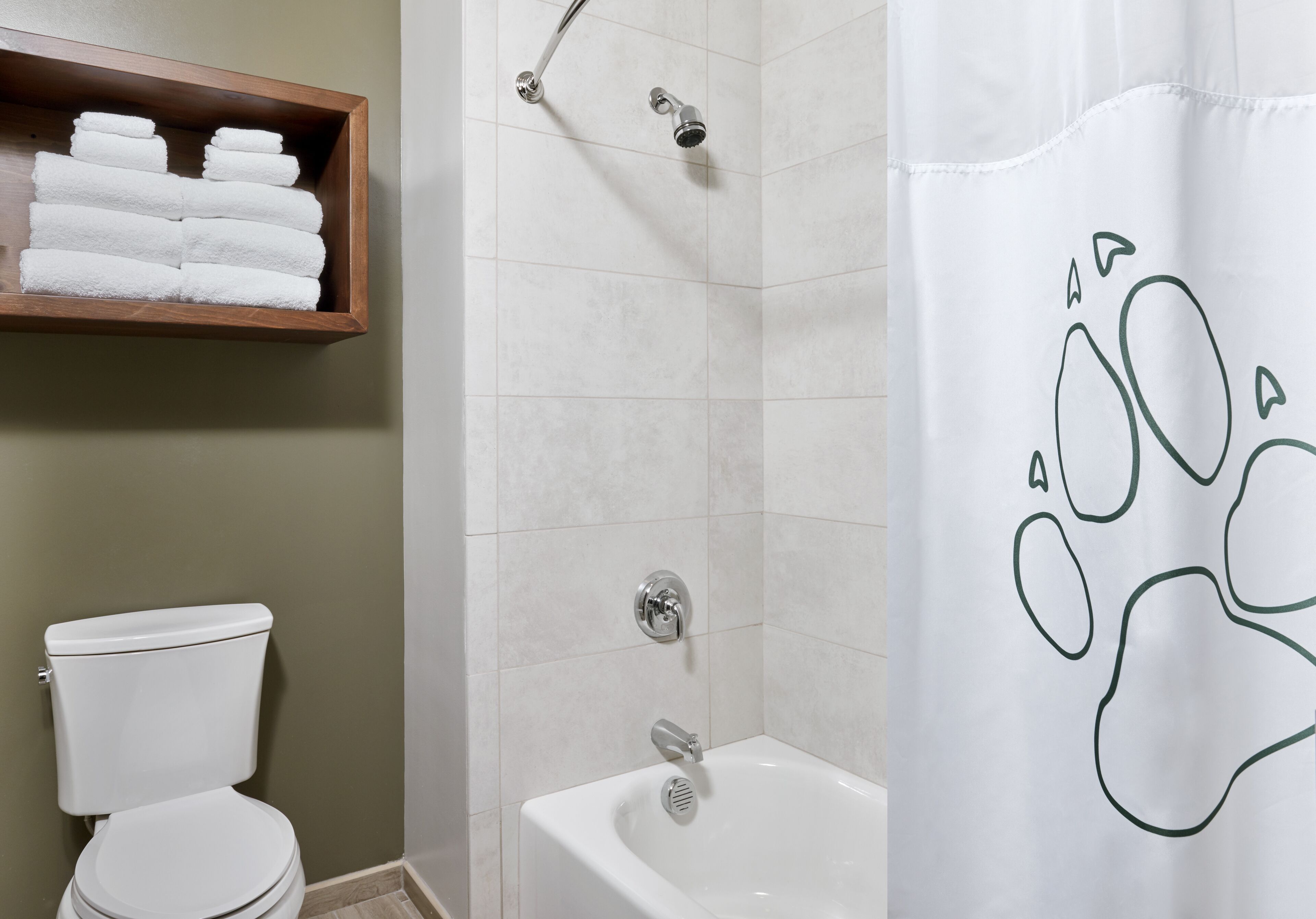 A bathroom with a toilet, a shower with a glass door, and a shelf with folded towels.