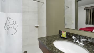 A bathroom with a white shower, a granite countertop sink, a mirror, and a towel rack.