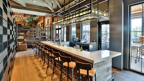 A modern bar area with a long counter, multiple stools, and a view through large windows. - Great Wolf Lodge Arizona (Scottsdale)