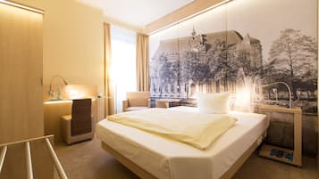 A hotel room with a large bed, a desk, a chair, a lamp, and a wall-mounted TV.