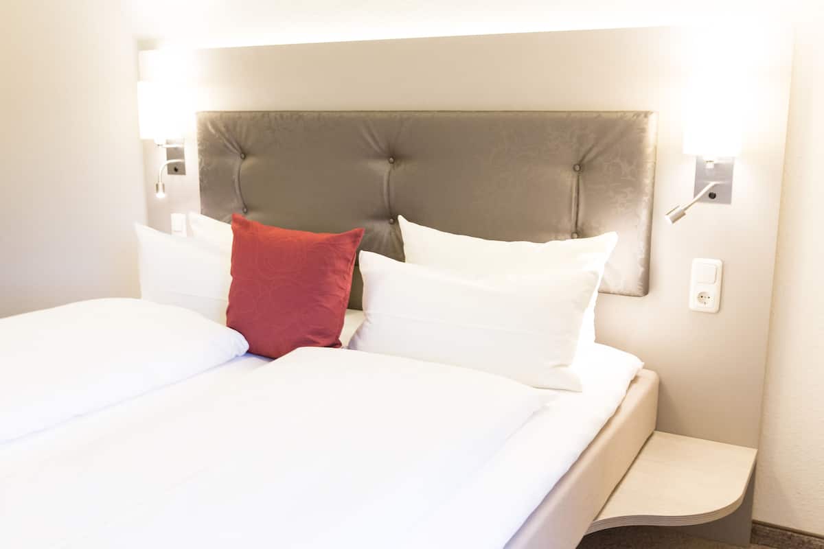 A neatly made bed with white and red pillows, a tufted headboard, and a bedside table with a lamp.