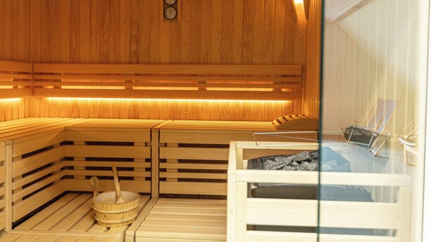 Una sauna con bancos de madera y un cubo de madera con una cuchara de madera.