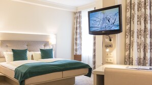 Una habitación de hotel con cama, televisor montado en la pared y escritorio con silla.