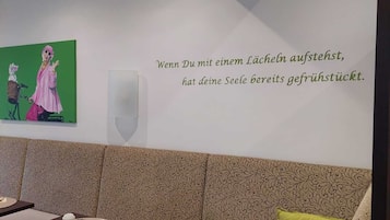 Uma sala de jantar com uma mesa posta para dois, uma parede com uma citação em alemão e um quadro verde acima da mesa.
