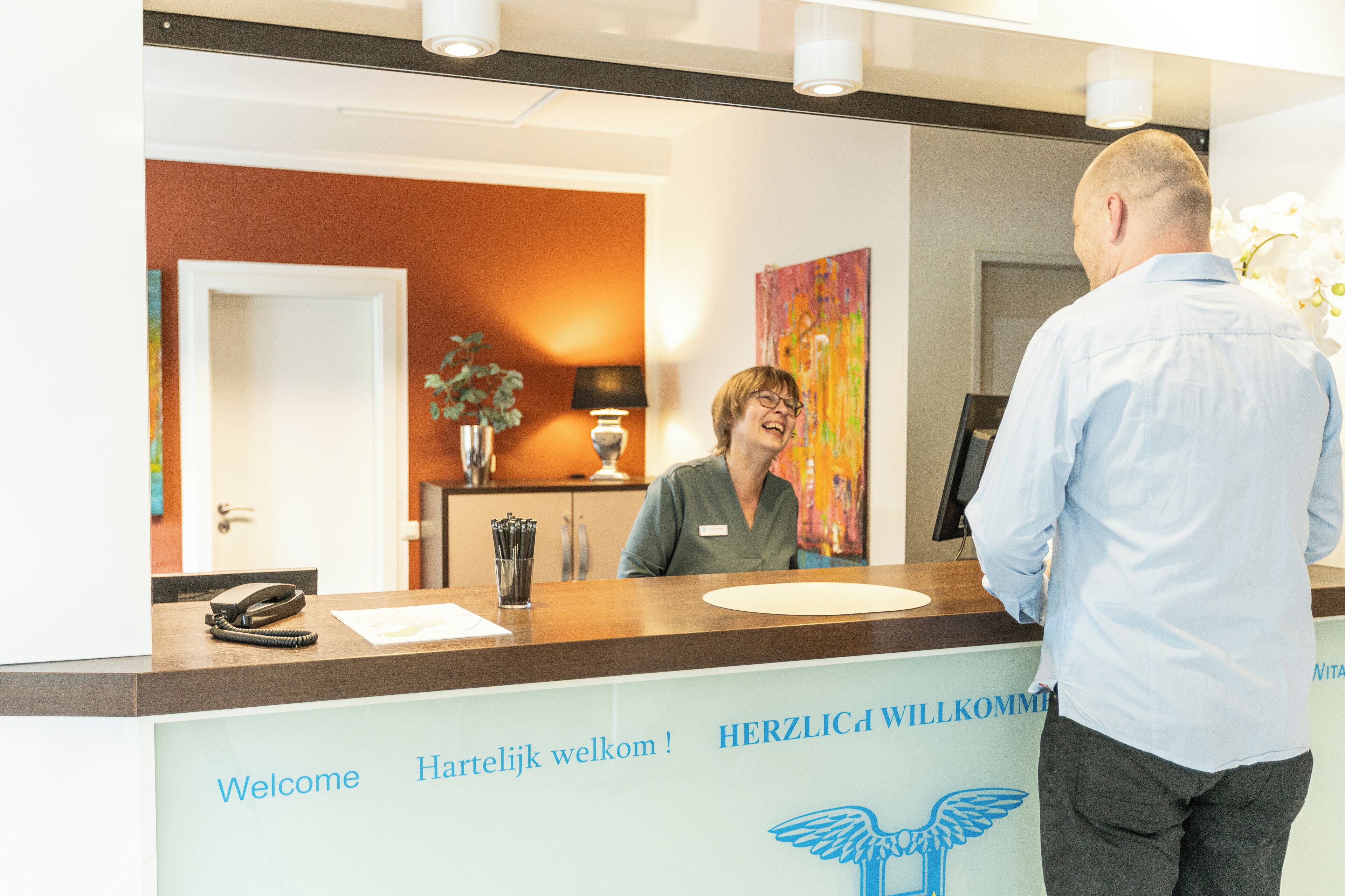 En receptionsdisk med skilte, der viser 'Welcome' og 'Herzlich willkommen' i en hotellobby.