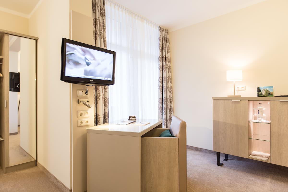 A hotel room with a television mounted on the wall, a desk with a lamp, and a cabinet with glass doors.