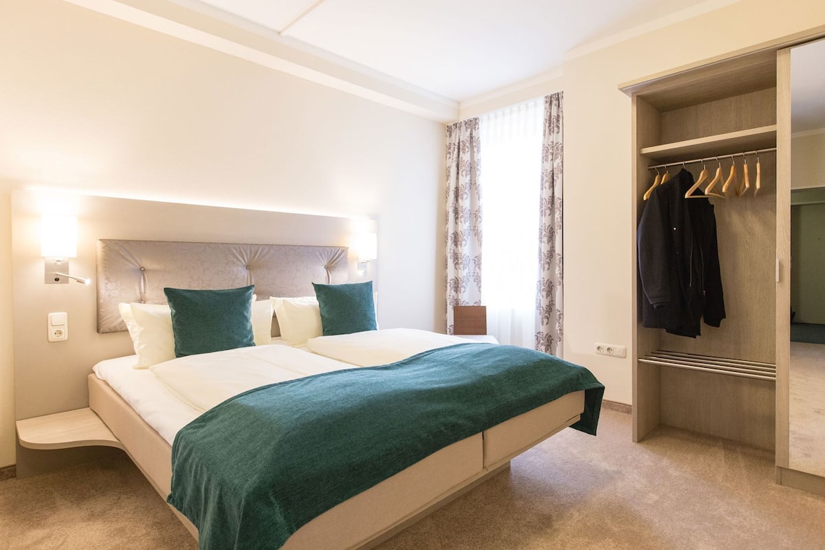 A hotel room with a bed, bedside tables, a wardrobe, and a window with curtains.