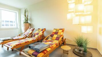 A room with three wooden sun loungers, a small table, and a potted plant.