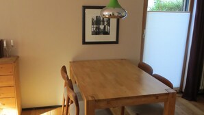 Ein Essbereich mit Holztisch und Stühlen, einem gerahmten Bild an der Wand und einem Fenster mit Blick auf Grünflächen.