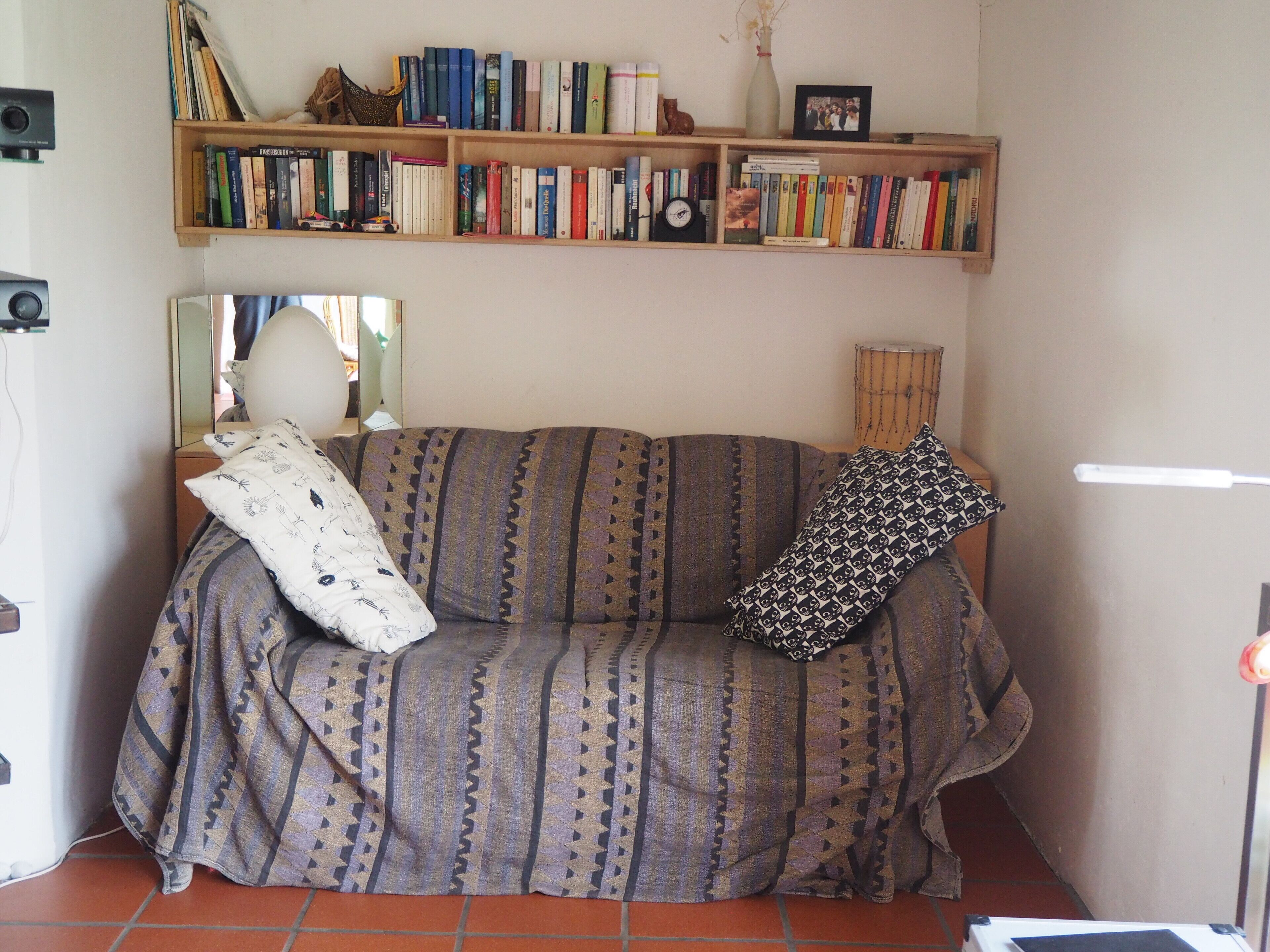 Un salon avec un canapé, des coussins, une bibliothèque et un miroir.