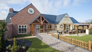 A brick building with a large clock, a covered patio area with outdoor seating, and a well-maintained lawn. - Pine Marten, Dunbar by Marston's Inns (Dunbar)