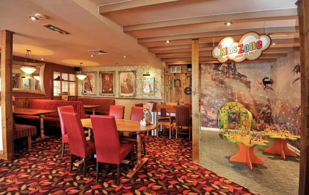 En restaurang med ett särskilt område för barn, med bland annat ett lekbord och en väggmålning med dinosauriemotiv.