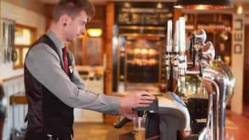 A barista operating a coffee machine in a cafe with a visible espresso machine and a glass of coffee being prepared.